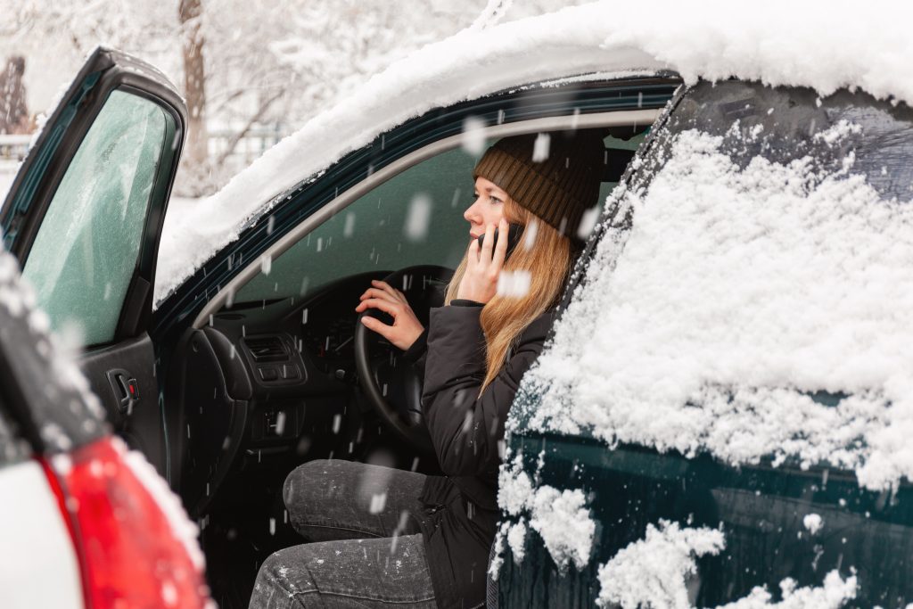 IMPLEMENTING EFFECTIVE ON-HOLD STRATEGIES - Young woman calling for help or assistance inside snow covered car.  Engine start in frost. Breakdown services in the winter. blizzard disaster relief - on hold marketing concept