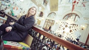 Woman sitting on bench in shopping mall looking up at decorations and listening to overhead music and announcements with winter holiday decorations in the background.