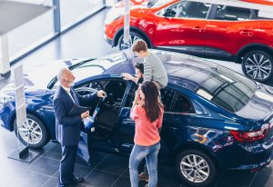 The strategic use of overhead marketing in car dealerships can transform the customer experience, making it more engaging and enjoyable - overhead view of salesman showing car to family in dealership showroom