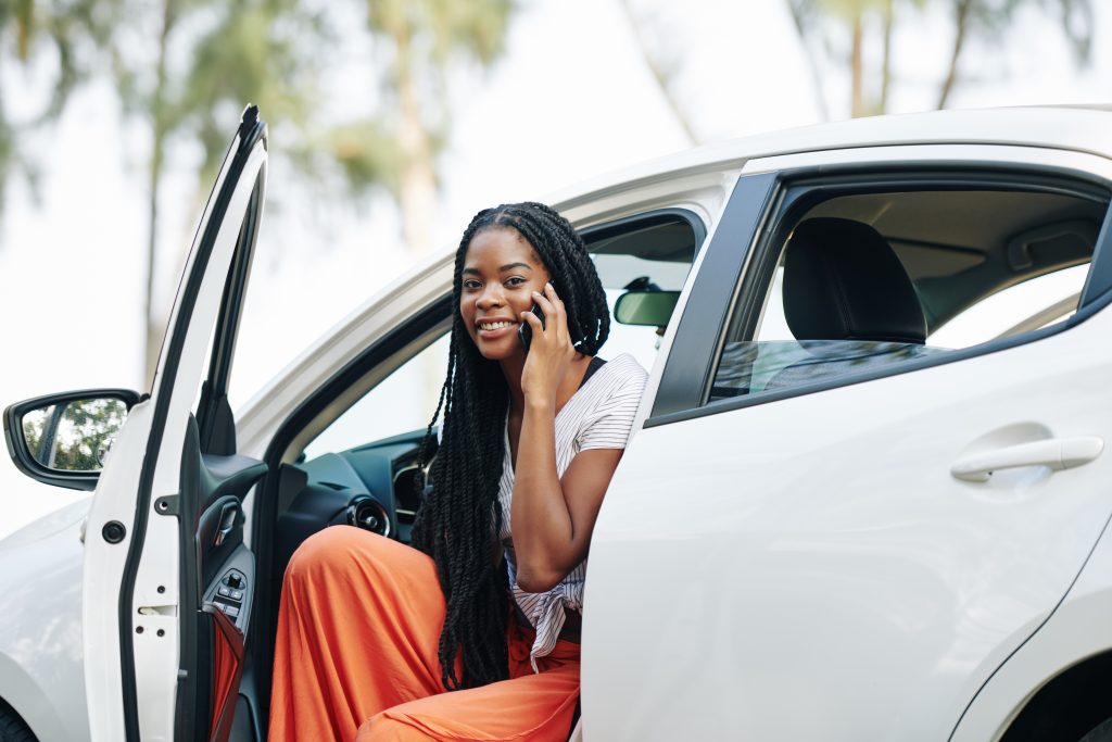 On-hold music and messaging are more than just background noise for waiting callers; they are essential tools for enhancing customer service, promoting sales, and building brand identity in the competitive car dealership industry - smiling woman getting out of car while talking on phone - strategic on-hold marketing concept showing benefits of effective on hold music and messaging