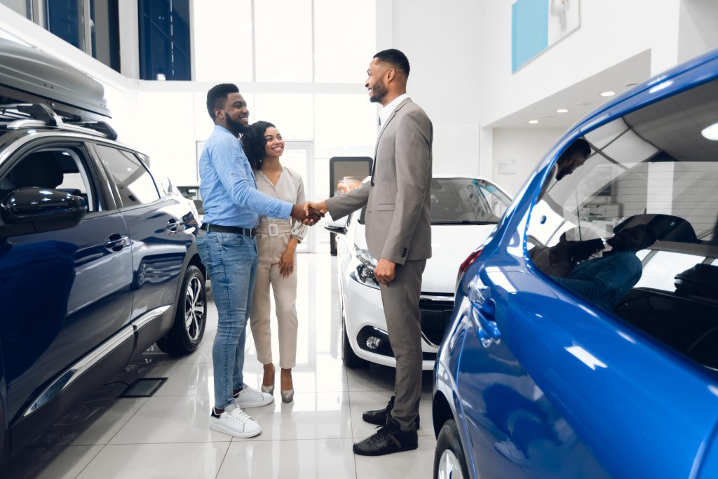 Well-chosen music and engaging messages can significantly reduce the perceived length of wait times - car salesman in dealership showroom shaking hands with smiling couple showing a successful sale - on-hold marketing concept showing the benefits of effective marketing 