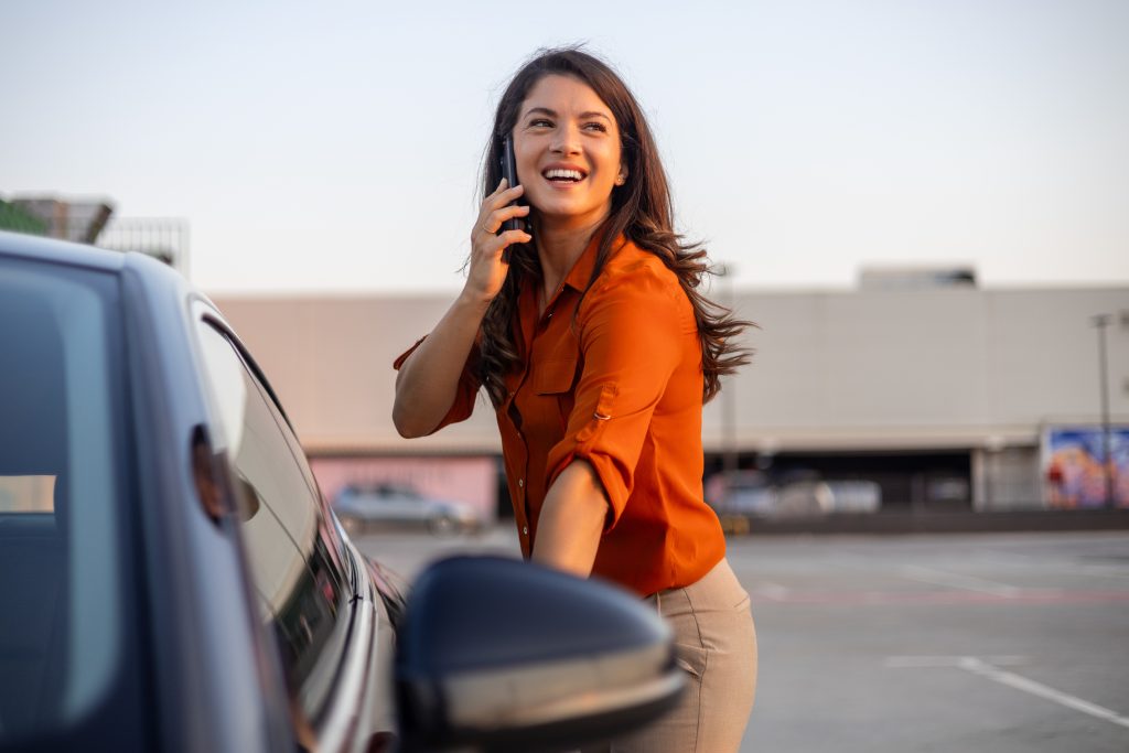 Setting the Tone with On-Hold Music - smiling woman getting into car in dealership lot, while talking on phone and looking into the distant - on-hold marketing concept for dealers