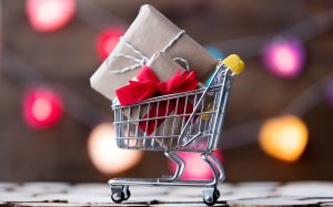 Shopping cart with Christmas and Black Friday gifts on color bokeh background