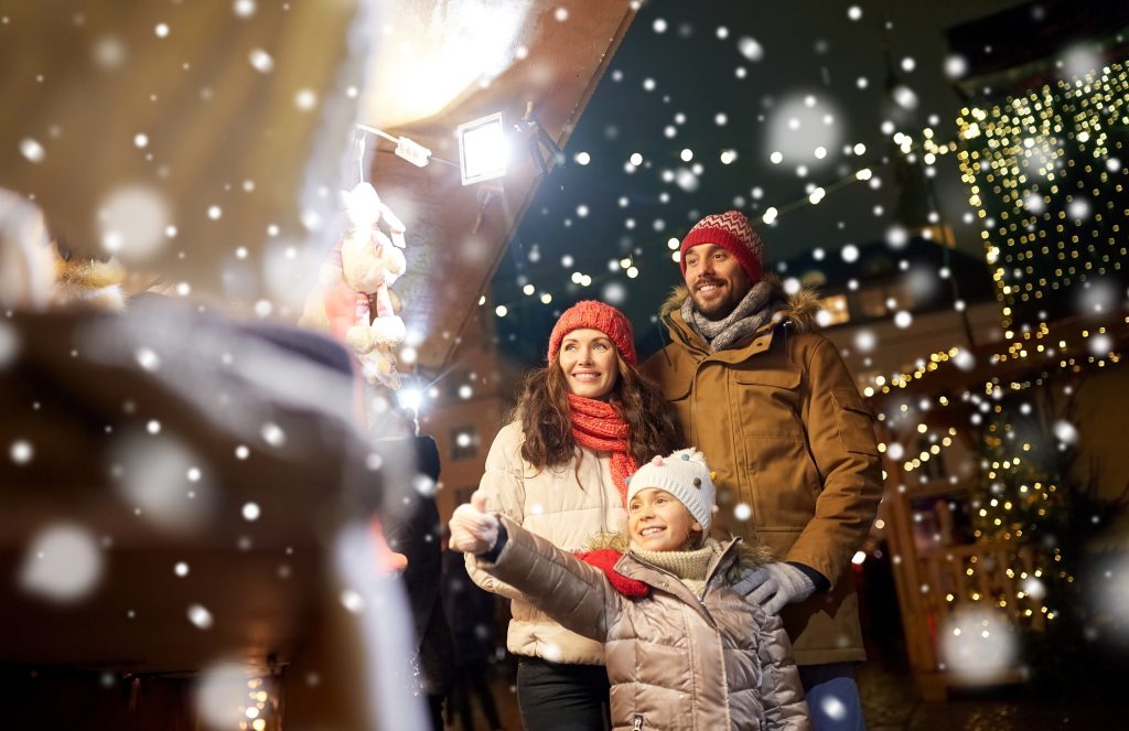 Happy family looking at holiday display in the snow surrounded by Christmas lights